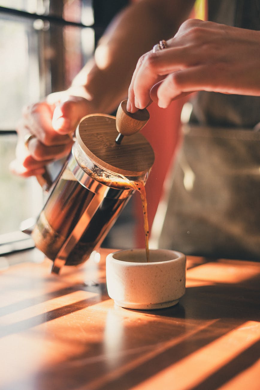 photo of person pouring brewed coffee on ceramic mug